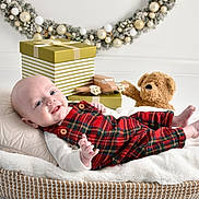 Leighton joined the competition — help win amazing prizes! baby, infant, plaid_overalls, smiling, basket, pillow, blanket, teddy_bear, toy_airplane, gift_box, holiday_wreath, decorations, indoor, cute, child, portrait, cozy, white_background, festive, happy