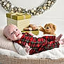 baby, infant, plaid_overalls, smiling, basket, pillow, blanket, teddy_bear, toy_airplane, gift_box, holiday_wreath, decorations, indoor, cute, child, portrait, cozy, white_background, festive, happy
