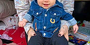 Rossi is registered to the contest to win money with this photo: baby, infant, smiling, beanie, denim_jacket, cowboy_boots, socks, adult_hands, sweater, seated, toys, blanket, play_area, portrait, happy, cute, clothing, indoor, family, nursery
