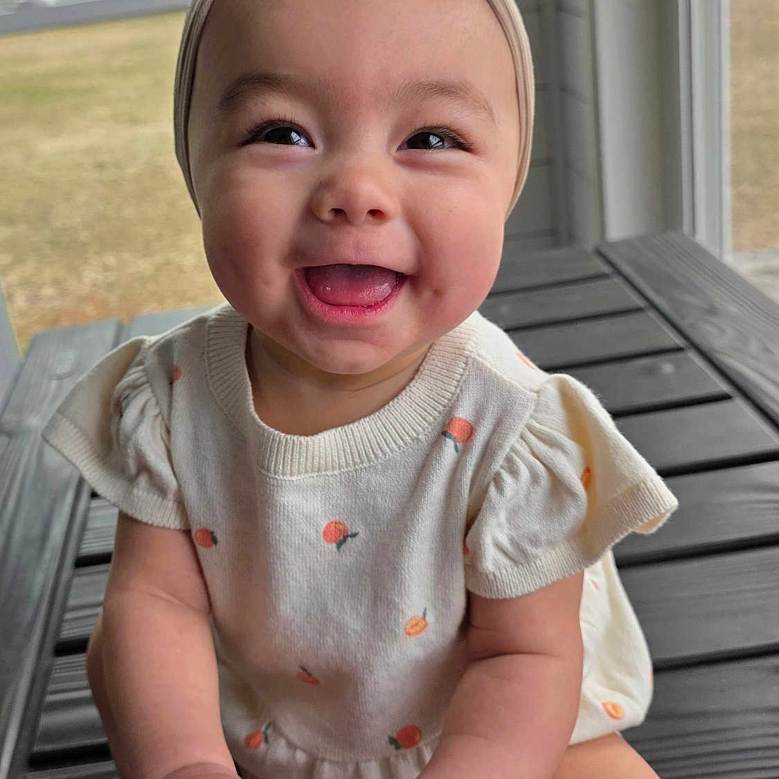 Rossi is registered to the contest to win money with this photo: baby, chubby_cheeks, close_up, cute, hands, happy, headband, infant, milestone_disc, natural_light, onesie, outdoor_background, porch, portrait, seven_months, sitting, smile, tongue, window, wooden_toy
