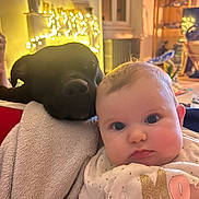 Ambre a rejoint le concours — aidez-le/la à gagner de superbes lots ! baby, infant, dog, black_dog, pet, blanket, fairy_lights, bokeh, living_room, cozy, cheeks, close_up, portrait, cuddling, sofa, onesie, indoor, cute, companion, relaxed