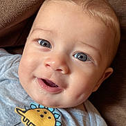 Leo is registered to the contest to win money with this photo: baby, child, smiling, face, blue_eyes, drool, dinosaur, shirt, hello, clothing, cute, close_up, infant, person, couch, brown, happy, indoors, portrait, young