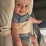 baby, infant, smile, face, arm, leg, blue_clothing, onesie, cushion, bed, blanket, pointing, cheeky, happy, skin, person, indoor, young_child, head, cute