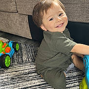 Matthew Gael is registered to the contest to win money with this photo: boy, car, casual, child, cute, face, floor, furniture, green_clothing, happy, head, home, indoor, person, playing, rug, smiling, sofa, toddler, toy