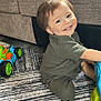 boy, car, casual, child, cute, face, floor, furniture, green_clothing, happy, head, home, indoor, person, playing, rug, smiling, sofa, toddler, toy