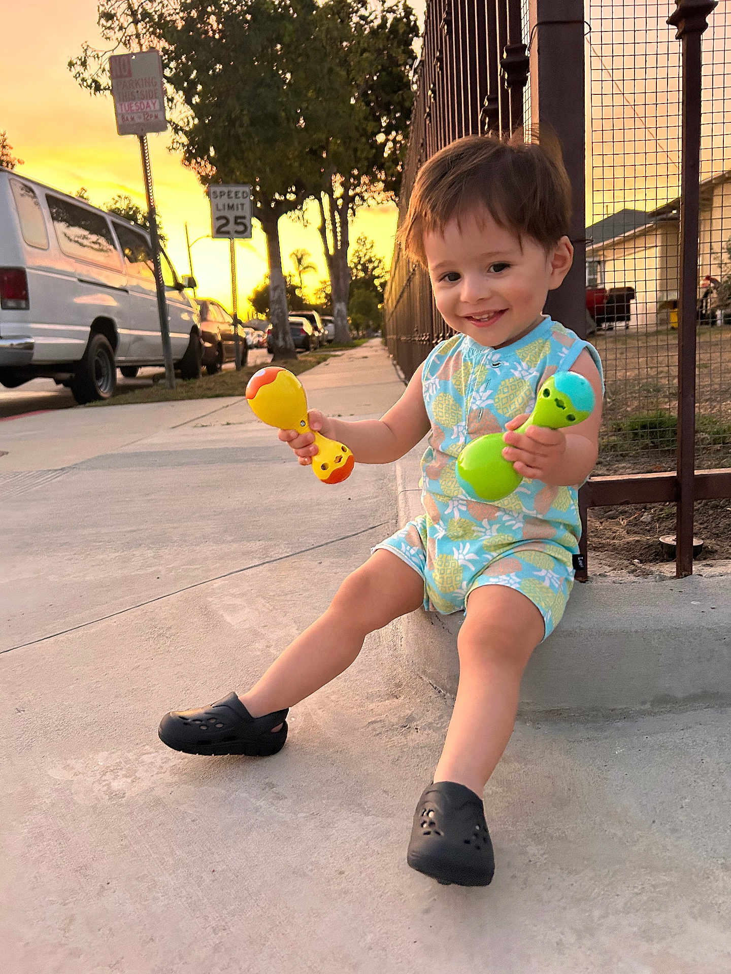 Matthew Gael is registered to the contest to win money with this photo: casual, child, clothing, cute, fence, footwear, happy, outdoor, person, play, rattle, sidewalk, smiling, street, sunset, toddler, toy, tree, urban, vehicle