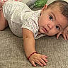 baby, crawling, floral_onesie, curious, couch, hand, red_bracelet, face, eyes, infant, skin, person, indoors, closeup, expression, child, young, comfortable, home, texture