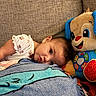 baby, child, plush_toy, blanket, couch, sofa, indoor, resting, cute, comfort, colorful, soft, toy, face, person, head, happy, smiling, cozy, home