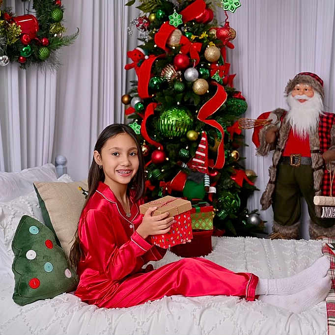 Siena joined the competition — help win amazing prizes! bed, celebration, child, christmas, christmas_tree, cushion, festive, gift_box, girl, holiday, holiday_decorations, indoors, pajamas, plaid_blanket, present, red_clothing, santa_decoration, smiling, white_bedspread, wreath