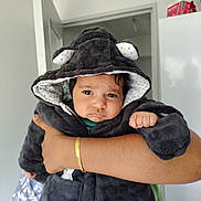 Aryan Samarasinghe a rejoint le concours — aidez-le/la à gagner de superbes lots ! baby, infant, hooded_jacket, plush, adorable, serious_expression, brown_eyes, parent_hand, gold_bracelet, indoor, doorway, refrigerator, portrait, closeup, soft_texture, warm_clothing, skin, small_fist, holding, home_interior