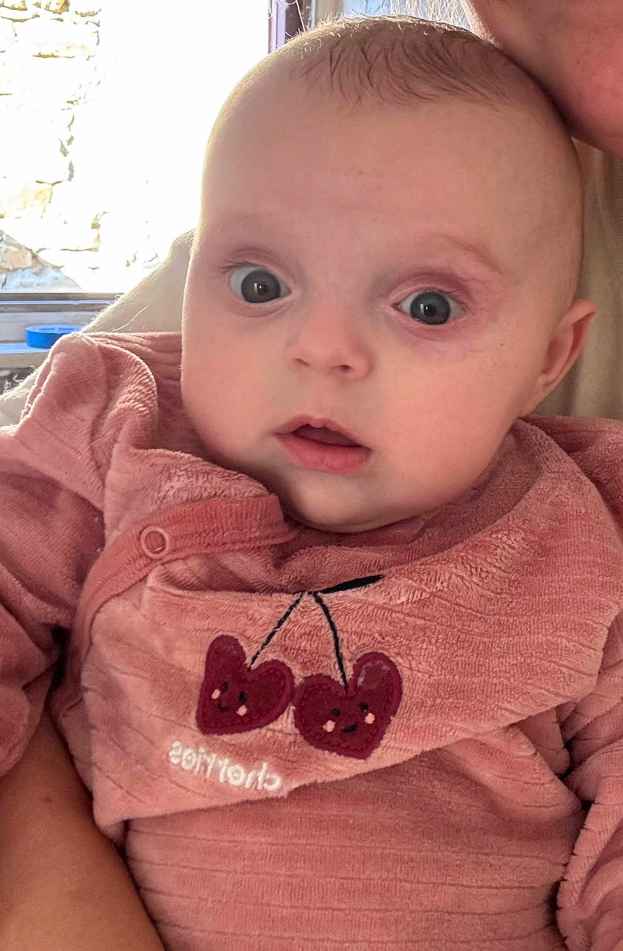 Andrea participe au concours pour gagner de l'argent avec cette photo : baby, child, infant, face, eyes, pink_clothing, cherry_embroidery, person, portrait, closeup, curious, indoor, window, adult, holding, soft_light, skin, expression, cute, young