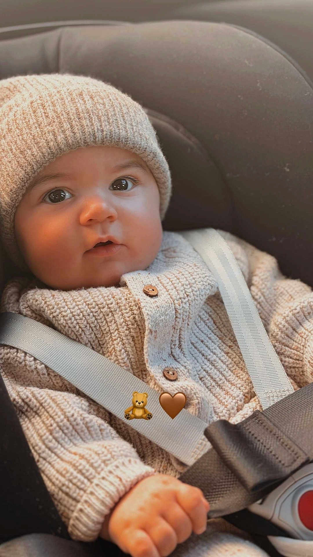 Solann a rejoint le concours — aidez-le/la à gagner de superbes lots ! baby, child, car_seat, knit_hat, knit_sweater, seatbelt, straps, closeup, portrait, cute, indoor, infant, hand, face, eyes, warm_lighting, soft_texture, buttoned_clothing, cozy, young