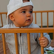 Solann participe au concours pour gagner de l'argent avec cette photo : baby, backwards_cap, cap, cheeks, closeup, crib, cute, eyes, face, grip, hand, indoor, infant, neutral_expression, portrait, sitting, soft_lighting, sweater, toddler, wooden_rail