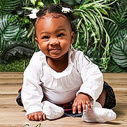 Skyler is registered to the contest to win money with this photo: baby, child, girl, smiling, white_bows, white_top, plaid_skirt, sitting, wooden_floor, green_plants, leafy_background, portrait, cute, happy, indoor, person, infant, crawling, face, closeup