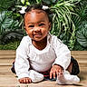 baby, child, girl, smiling, white_bows, white_top, plaid_skirt, sitting, wooden_floor, green_plants, leafy_background, portrait, cute, happy, indoor, person, infant, crawling, face, closeup
