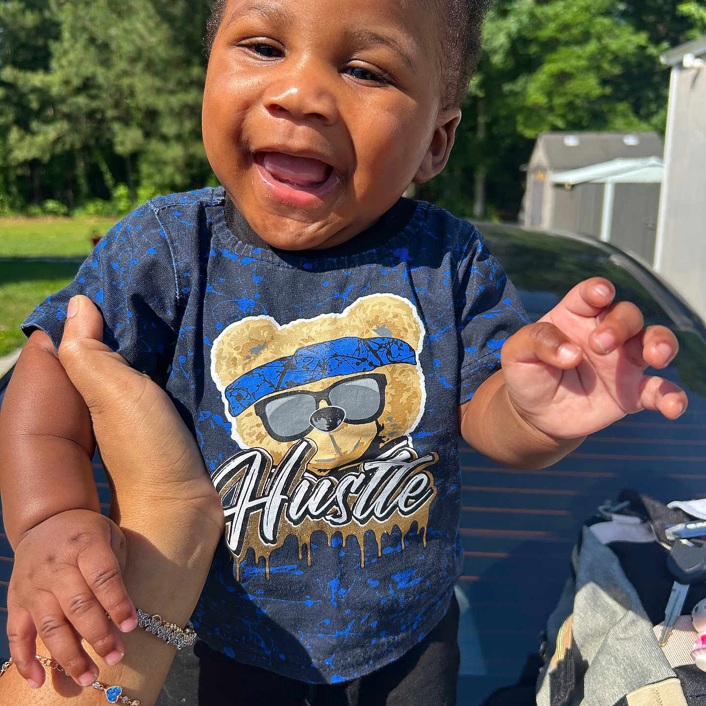Elijah is registered to the contest to win money with this photo: toddler, child, smiling, happy, outdoor, sunlight, hand, person, bear_graphic, tshirt, clothing, shorts, nature, trees, car, backpack, portrait, baby, cute, daytime