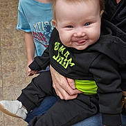 Nevaeh joined the competition — help win amazing prizes! baby, child, toddler, infant, smiling, tongue_out, black_clothing, blue_shirt, adult_hand, sitting, indoor, floor, red_chair, jeans, sneakers, person, portrait, cute, happy, family