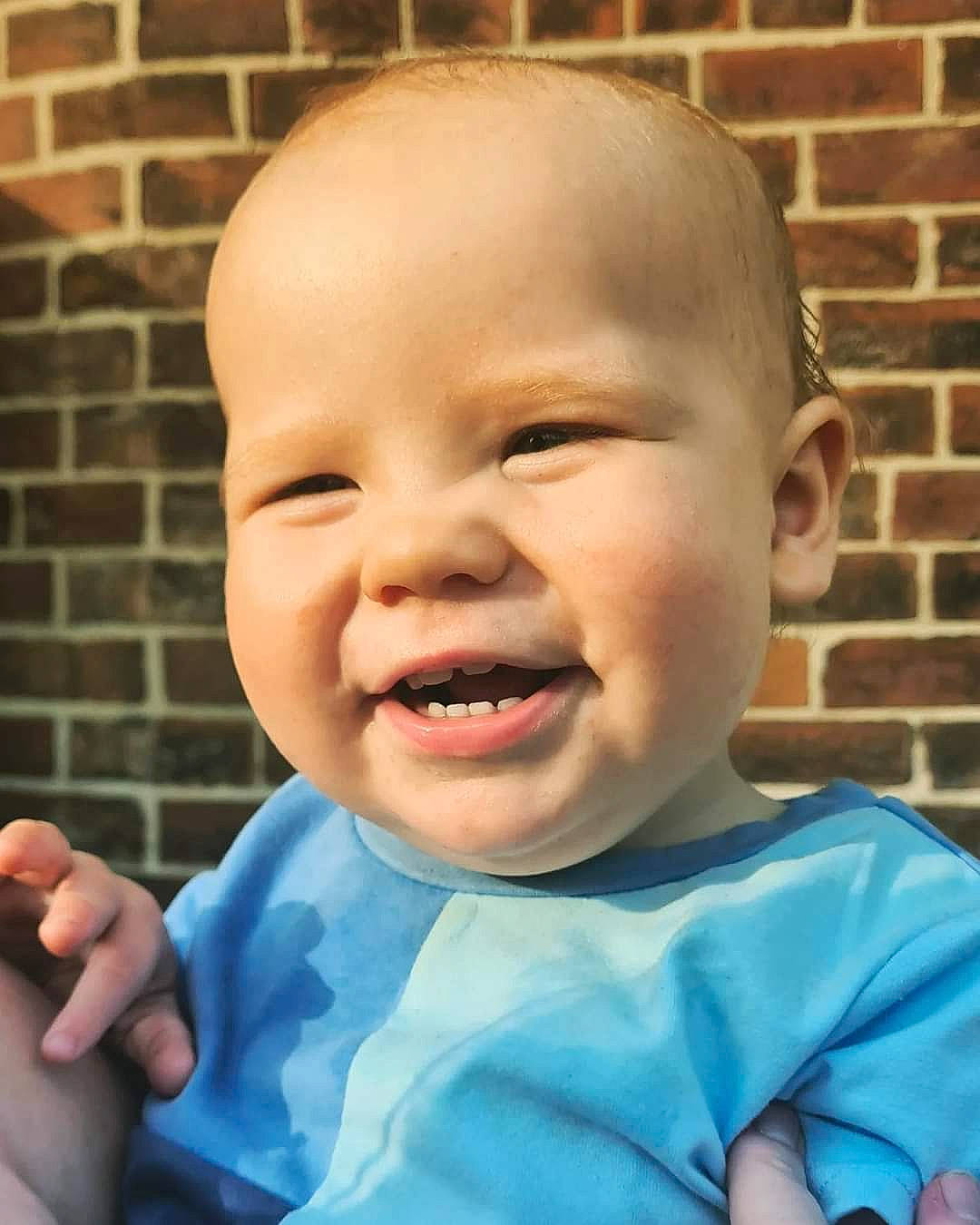 Freddie is registered to the contest to win money with this photo: baby, baby_laughing, baby_toddler_clothing, brick, brickwork, cheek, chin, eye, finger, gesture, happy, head, iris, lip, mouth, nose, person, skin, sleeve, smile