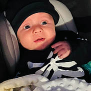 Lukas E joined the competition — help win amazing prizes! baby, infant, blanket, hat, clothing, face, person, portrait, child, dark_background, cute, cozy, expression, indoors, newborn, soft_texture, warm, wrapped, sitting, black_clothing