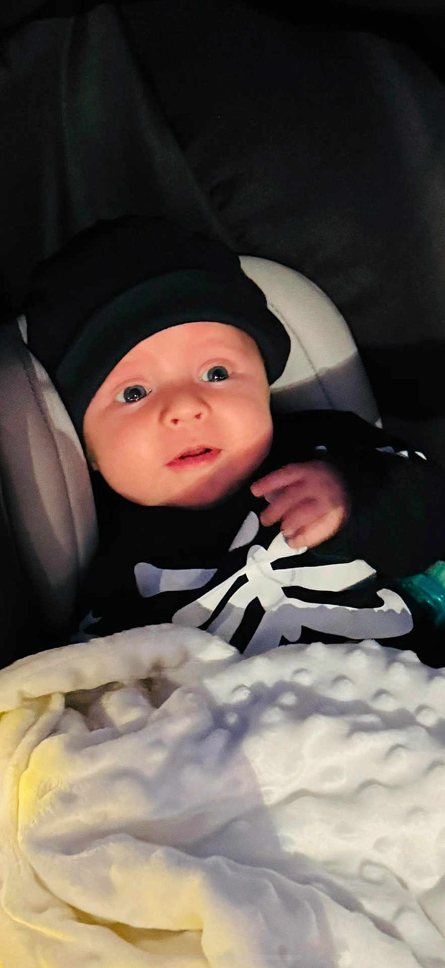 Lukas E joined the competition — help win amazing prizes! baby, infant, blanket, hat, clothing, face, person, portrait, child, dark_background, cute, cozy, expression, indoors, newborn, soft_texture, warm, wrapped, sitting, black_clothing