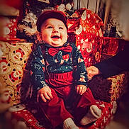 Marceau participe au concours pour gagner de l'argent avec cette photo : baby, child, christmas, holiday, presents, gifts, tree, smiling, happy, red_clothing, bow_tie, cap, sitting, indoors, festive, celebration, decorations, sock, person, portrait