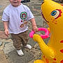 Paddy is registered to the contest to win money with this photo: barefoot, casual_clothing, child, curly_hair, cute, fence, garden, green_tricycle, holding_hands, inflatable_toy, khaki_pants, outdoor, playground, playtime, smiling, stone_patio, toddler, toy_car, white_tshirt, yellow_dinosaur