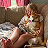 animal, barefoot, blond_hair, casual, child, comfort, controller, couch, curtains, dog, home, human, indoor, living_room, pet, pillow, red_curtains, relaxed, seated, shiba_inu