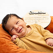 Alexandre Fares a rejoint le concours — aidez-le/la à gagner de superbes lots ! baby, newborn, smile, infant, cushion, orange, mustard, clothing, face, portrait, cute, resting, wooden_sign, text, birth_details, cozy, indoors, happy, child, person
