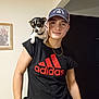Bella is registered to the contest to win money with this photo: young_man, dog, indoor, black_tshirt, adidas_logo, baseball_cap, pet_on_shoulder, portrait, casual_clothing, bracelets, chain_necklace, framed_picture, light_skin, short_sleeves, black_door, small_dog, looking_at_camera, friendly, human, animal
