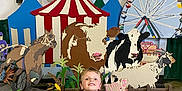Bentlee joined the competition — help win amazing prizes! child, boy, smiling, sitting, floor, concrete, dinosaur_shirt, carnival, circus_tent, animal_cutouts, cow, horse, pig, goat, ferris_wheel, background, indoor, colorful, playful, decorations
