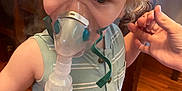 Luke is registered to the contest to win money with this photo: toddler, child, nebulizer, mask, medical_device, curly_hair, blonde_hair, striped_shirt, sleeveless, indoor, hand_holding, wooden_floor, person, healthcare, respiratory, closeup, young_child, support, treatment, home