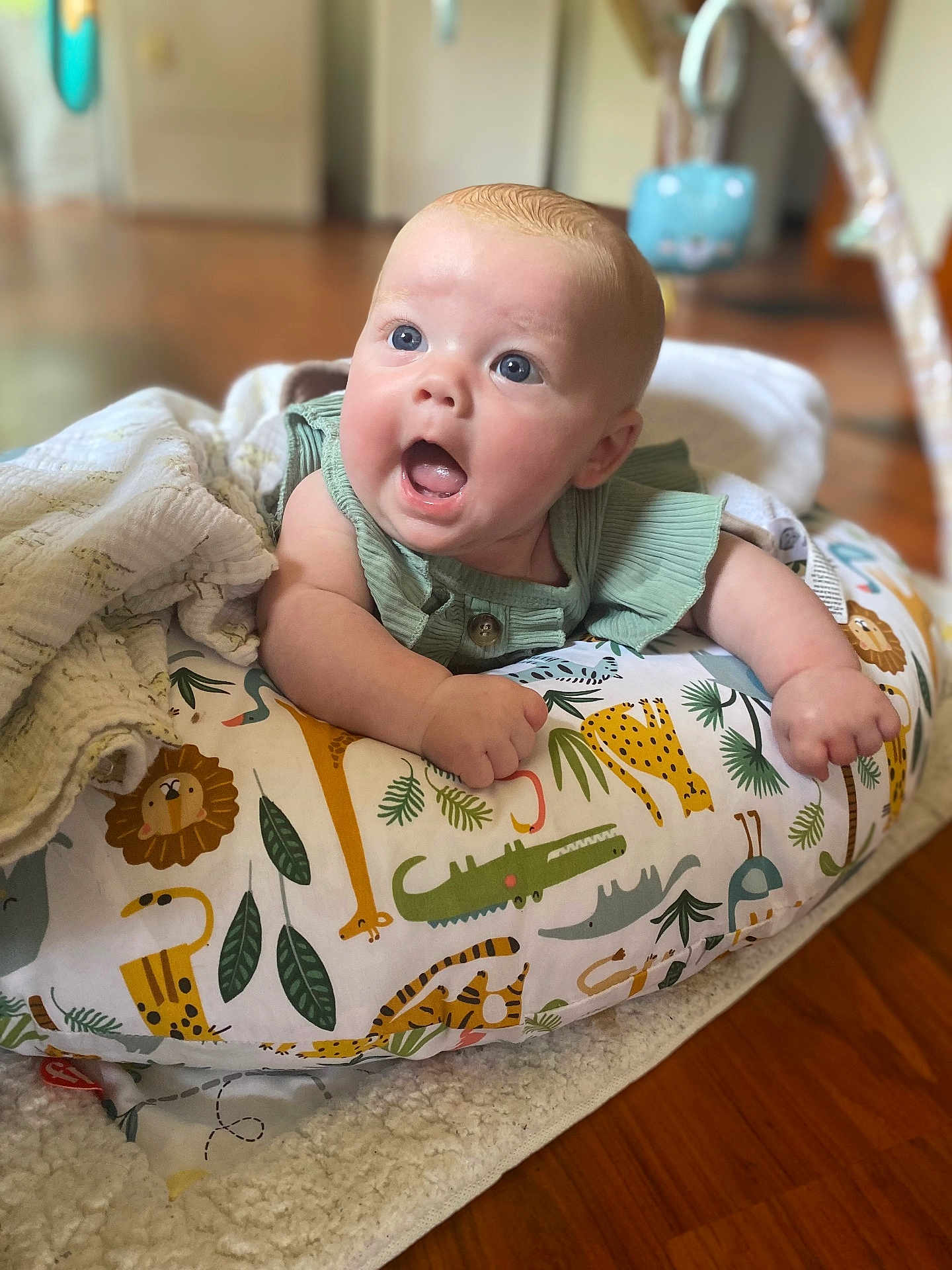 Valerie is registered to the contest to win money with this photo: baby, infant, cute, surprised, expression, cushion, animal_print, blanket, floor, wooden_floor, indoors, child, portrait, closeup, blue_eyes, green_clothing, tummy_time, play_area, home, soft_texture