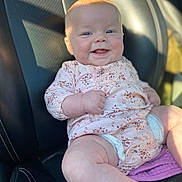 Valerie is registered to the contest to win money with this photo: baby, infant, smiling, happy, car_seat, clothing, floral_pattern, pink, skin, face, blue_eyes, chubby, cute, sunlight, comfort, leather, seat, hand, portrait, child