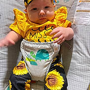 Penelope is registered to the contest to win money with this photo: baby, infant, child, yellow_clothing, sunflower_pattern, headband, bouncer, turtle_graphic, cute, chubby_cheeks, sitting, indoor, playful, colorful, soft_toys, fabric, person, young_child, comfortable, expression