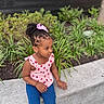 blue_jeans, casual_clothing, child, curly_hair, daylight, earrings, flowers, girl, greenery, hair, nature, outdoor, pink_bow, pink_top, plants, portrait, side_view, sitting, stone_ledge, young