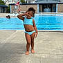 child, girl, swimming_pool, bikini, playful, pose, outdoor, summer, water, poolside, lifeguard, concrete, blue, person, curly_hair, casual, daytime, fun, recreation, vacation