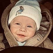 Ollie is registered to the contest to win money with this photo: baby, child, smiling, hat, knit_hat, pom_pom, jacket, brown_jacket, cute, portrait, face, happy, warm_clothing, closeup, infant, winter_clothing, baby_face, outdoor, baby_smile, childhood