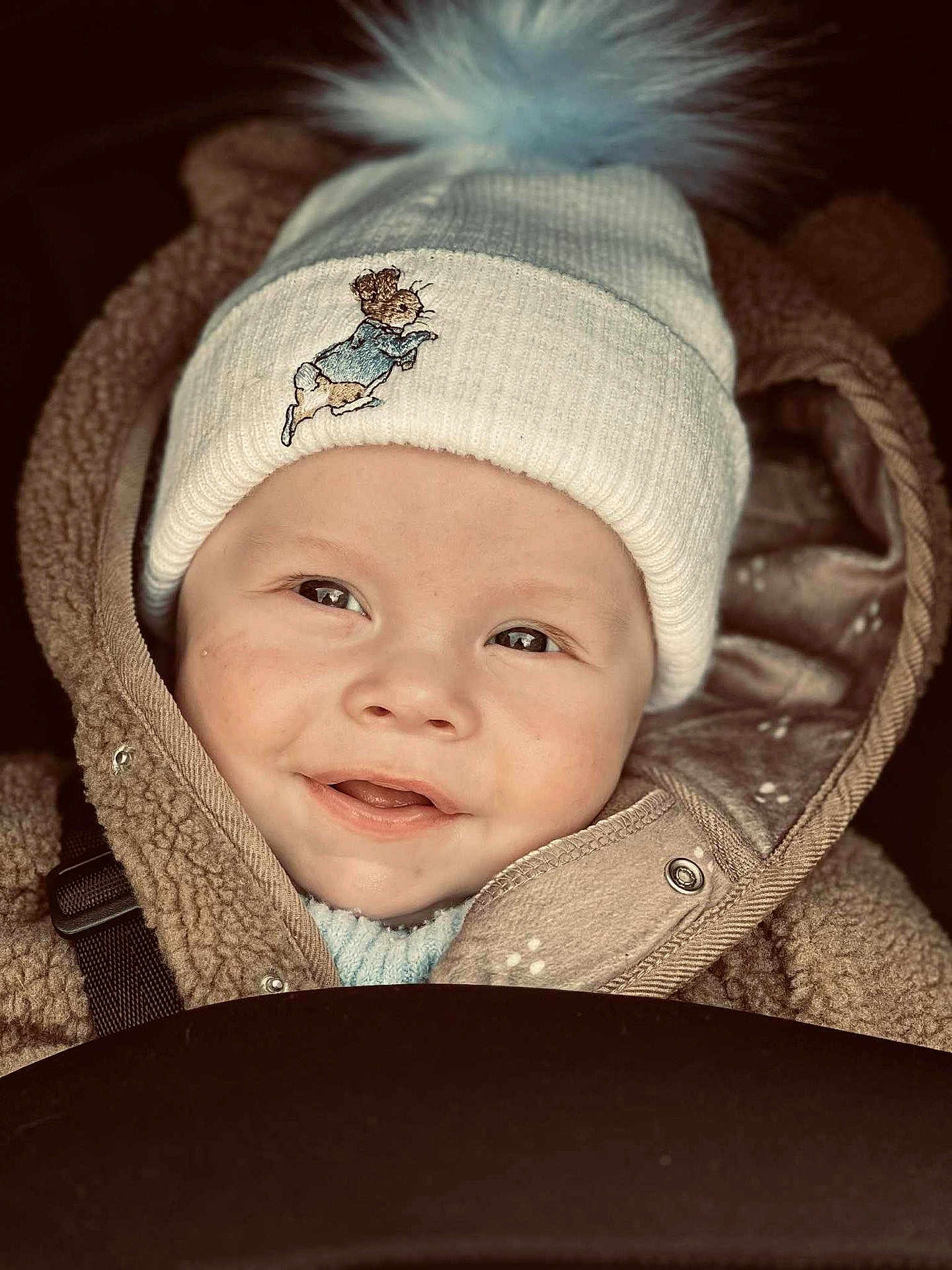 Ollie is registered to the contest to win money with this photo: baby, child, smiling, hat, knit_hat, pom_pom, jacket, brown_jacket, cute, portrait, face, happy, warm_clothing, closeup, infant, winter_clothing, baby_face, outdoor, baby_smile, childhood