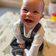 Ollie is registered to the contest to win money with this photo: baby, blurred_background, cheeks, child, close_up, cute, eyes, face, happy, infant, overalls, playmat, portrait, shallow_depth_of_field, sitting, smile, sock, tooth, toy, white_shirt
