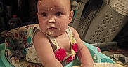 Ariel is registered to the contest to win money with this photo: baby, child, high_chair, food, messy, plate, hands, face, indoor, curious, clothing, colorful, kitchen, seat, candid, infant, exploring, cute, expression, furniture