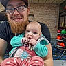 Ariel is registered to the contest to win money with this photo: man, baby, glasses, beard, pacifier, jacket, polka_dot, indoor, bowling_balls, table, chair, carpet, smile, holding, person, facial_hair, cap, playful, curious, casual