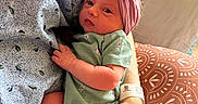 Evelynn is registered to the contest to win money with this photo: newborn, baby, infant, headband, green_clothing, adult_hand, hospital_wristband, patterned_pillow, indoor, cuddle, love, portrait, person, skin, face, hand, fabric, comfort, closeup, rest
