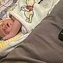 baby, sleeping, blanket, winnie_the_pooh, pillow, remote_control, bed, indoor, cozy, infant, child, resting, soft, comfort, cute, person, young_child, peaceful, nap, home