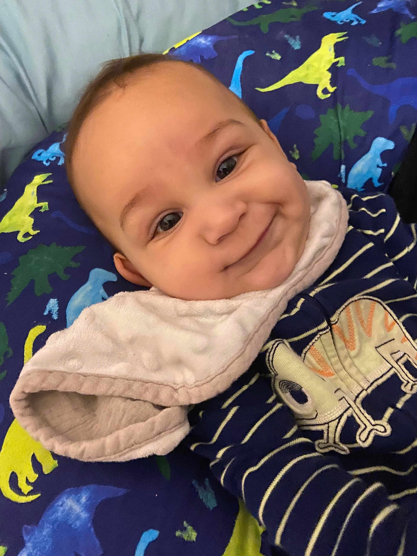 Bryan joined the competition — help win amazing prizes! baby, infant, smile, face, dinosaur_pattern, cushion, striped_clothing, bib, cheeks, cute, child, portrait, indoor, happy, young, person, closeup, soft_texture, blue, yellow