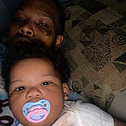 Janaya joined the competition — help win amazing prizes! baby, pacifier, adult, tattoo, face, portrait, curly_hair, indoor, pillow, pattern, closeup, person, sleepy, child, family, candid, casual, relaxed, skin, clothing