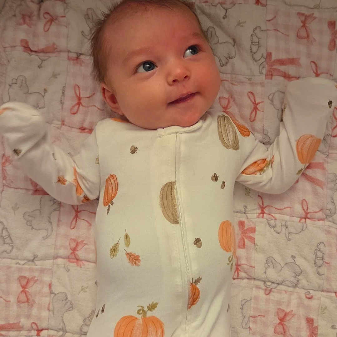 Ellee joined the competition — help win amazing prizes! adorable, baby, blanket, child, closeup, cozy, cute, face, home, infant, lying_down, onesie, pattern, pink, pumpkin, purple, quilt, sleepwear, smile, soft_toys