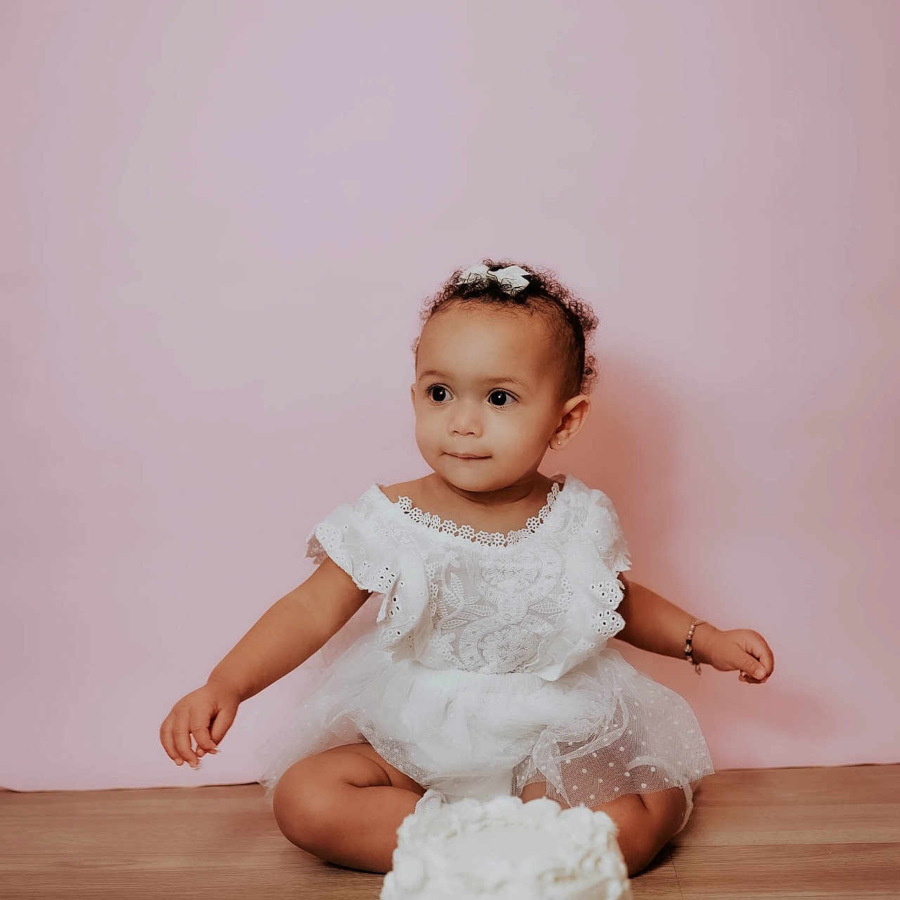 Willoh is registered to the contest to win money with this photo: birthday, bracelet, cake, celebration, child, curly_hair, cute, decorated_cake, happy, headband, indoors, lace, pink_background, portrait, sitting, smiling, toddler, white_dress, wooden_floor, young_child
