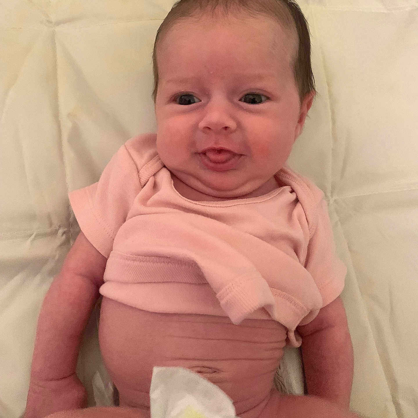 Everleigh-Marie is registered to the contest to win money with this photo: arm, baby, child, chubby, cute, diaper, expression, face, head, indoors, infant, lying_down, newborn, person, pink_shirt, skin, smile, soft_blanket, tongue_out, young