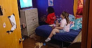Missy joined the competition — help win amazing prizes! bed, blanket, ceiling_fan, child, clothing, cup, curtain, dog, door, drawer, furniture, indoor, purple_wall, relaxed, room, sitting, television, toy, watching_tv, wooden_floor