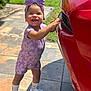 toddler, child, smiling, purple_bow, romper, sneakers, socks, car, red_car, outdoor, sunny, green_grass, patio, tiles, happy, standing, cute, playful, young_child, daylight